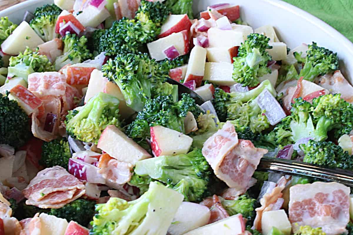 A close up look at a broccoli and apple salad with cooked bacon and red onion.