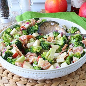 A vibrant broccoli and apple salad in a white bowl with a spoon.