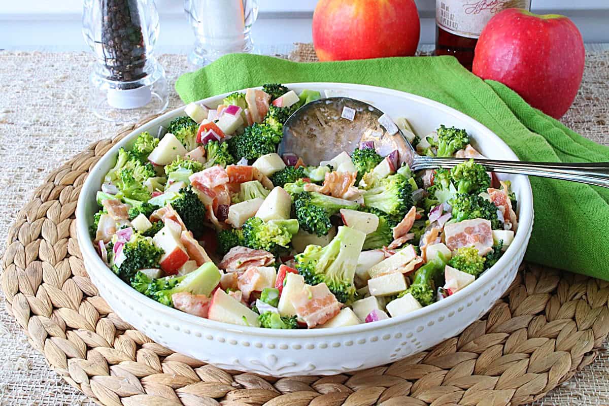 Bright green broccoli florets in a salad bowl along with bacon and apple pieces.