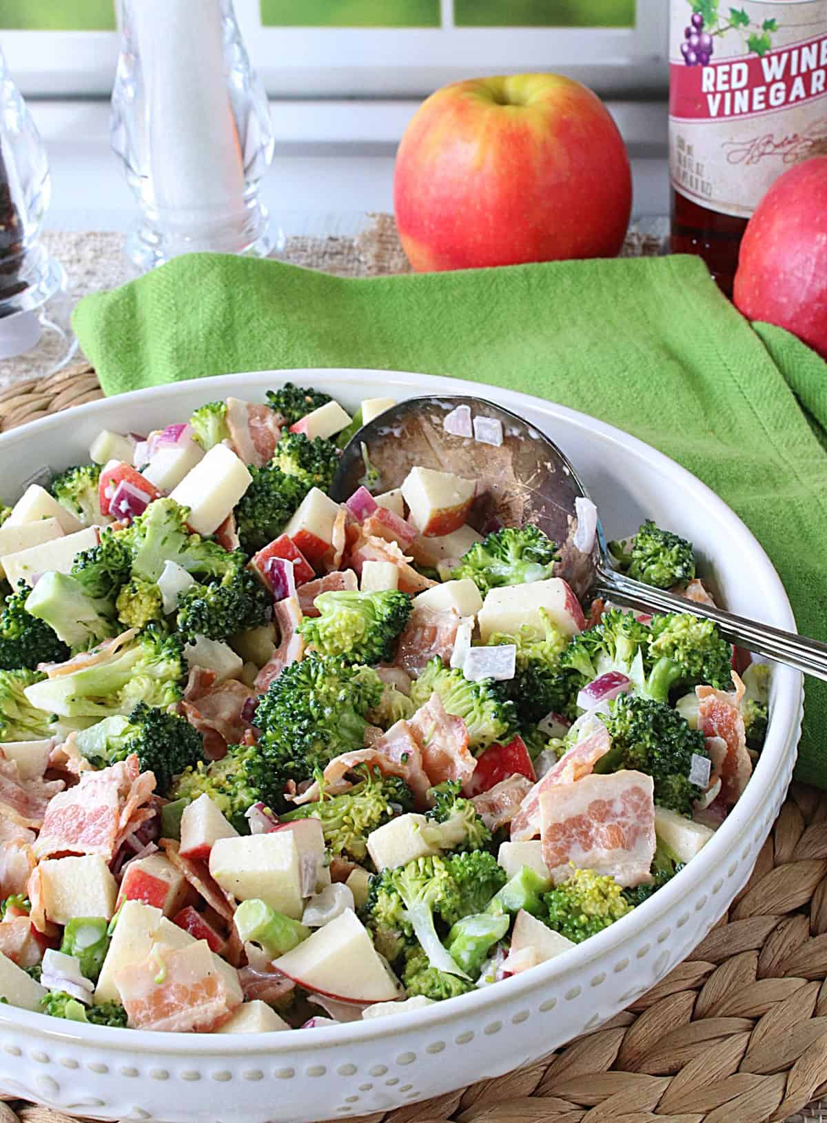 A green napkin in the background with a white bowl filled with broccoli apple salad in the foreground.
