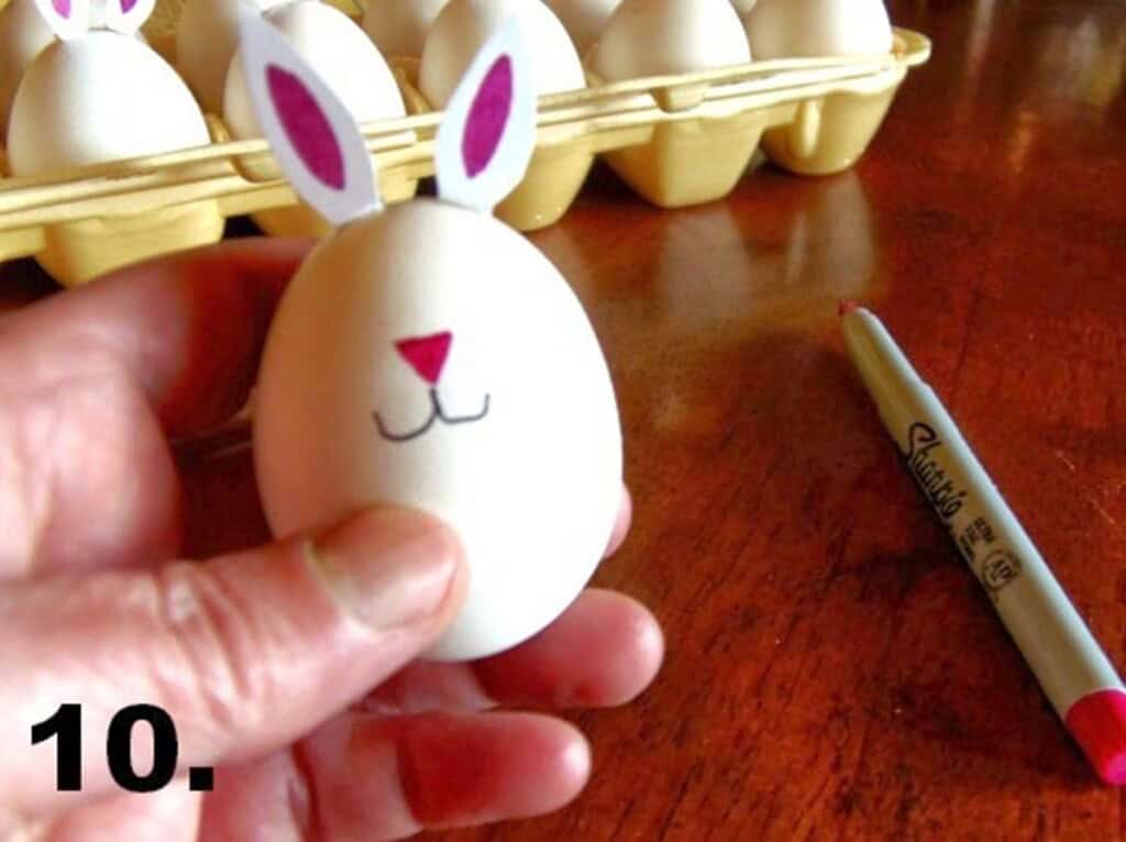 Hand holding a hard-boiled bunny egg with nose and mouth drawn on it.