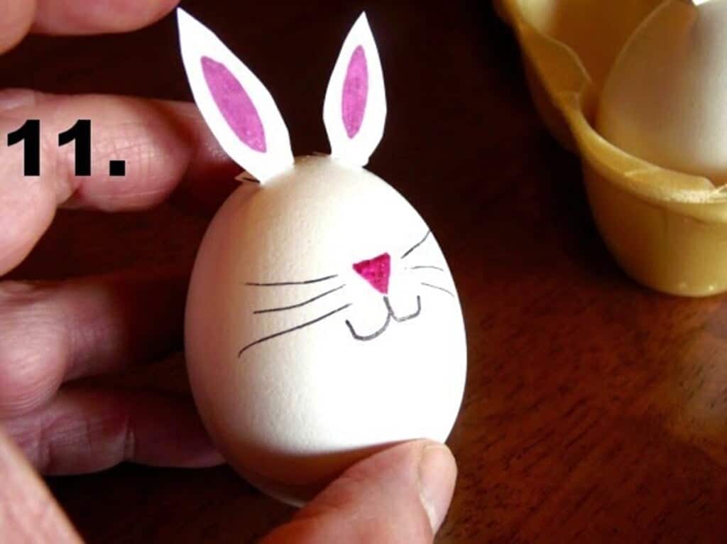 Hand holding a hard-boiled bunny egg with nose, whickers and mouth drawn on it.