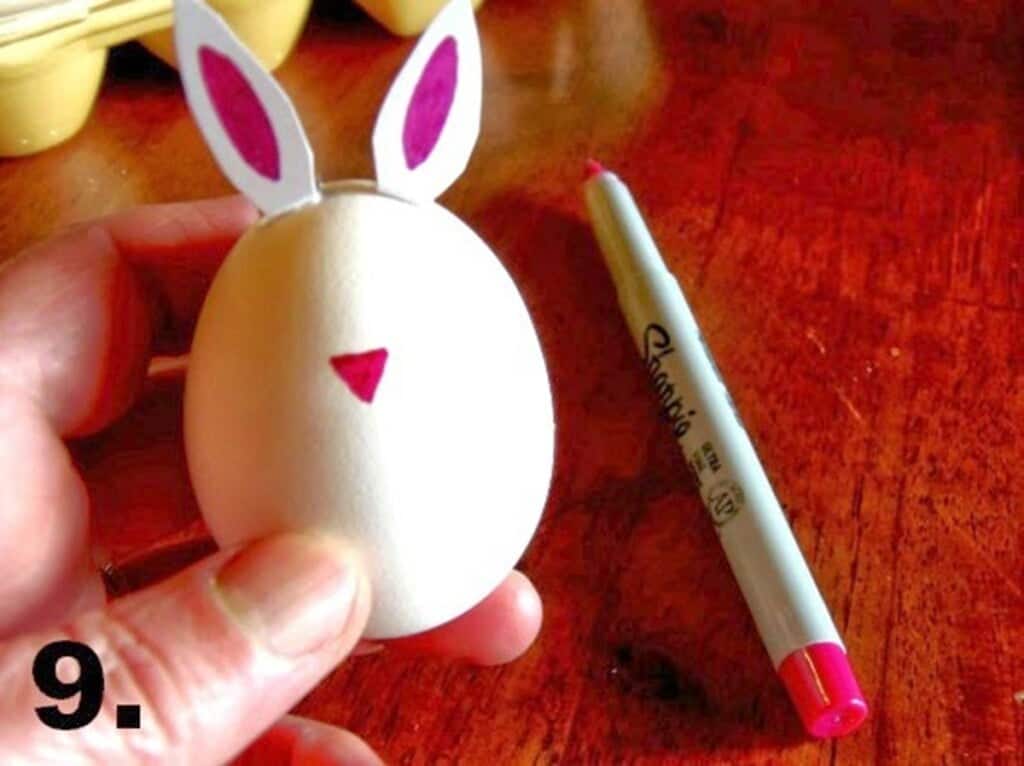Hand holding hard-boiled bunny egg with pink nose drawn on it.