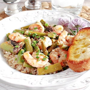 A pretty white bowl filled with Shrimp, asparagus and brown rice.