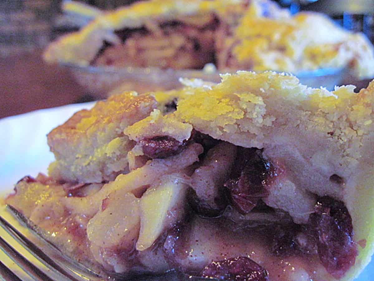 A slice of apple pear pie slice in the foreground with the entire pie in the background.