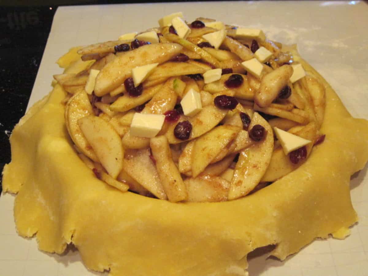 Apple and pear slices along with cranberries inside a pie crust bottom before baking.