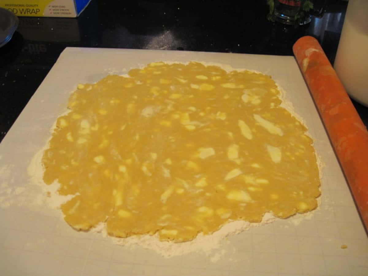 A rolling pie and a butter dotted homemade pie crust dough on a marble work surface.