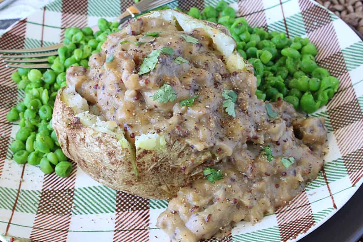 A delicious baked potato covered with brown bratwurst with gravy.