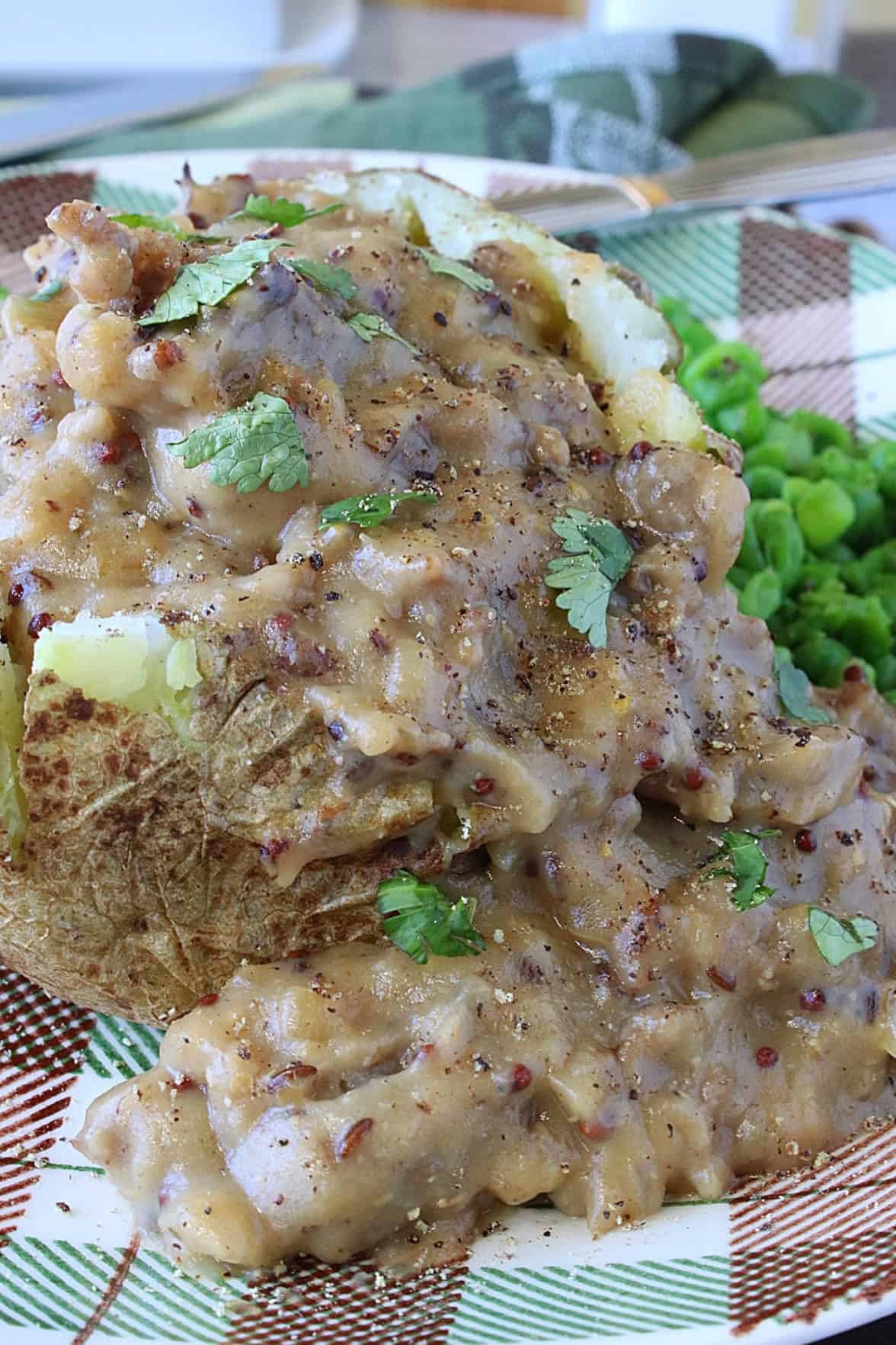 Thick bratwurst and gravy with parsley and mustard on top of a baked potato.