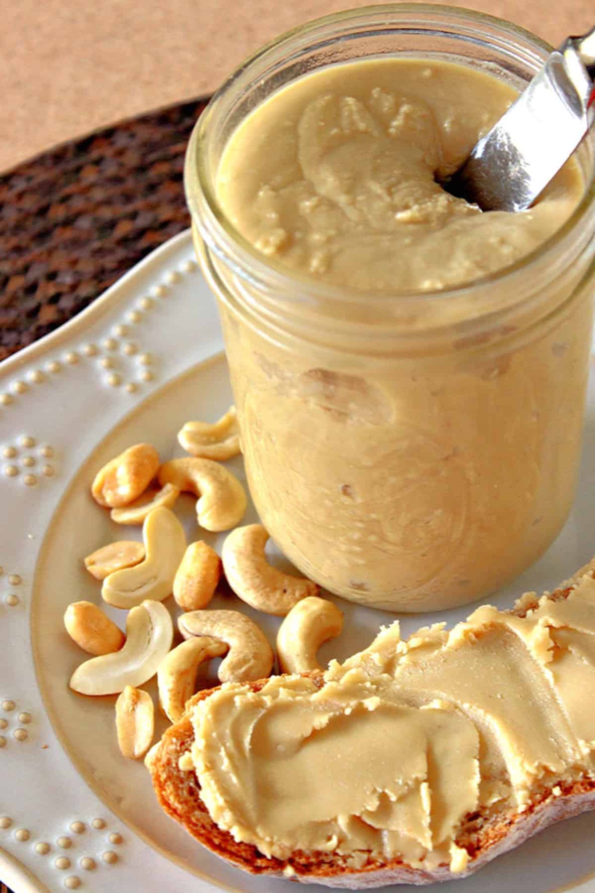 A glass jar filled with homemade peanut and cashew butter with a knife sticking out.