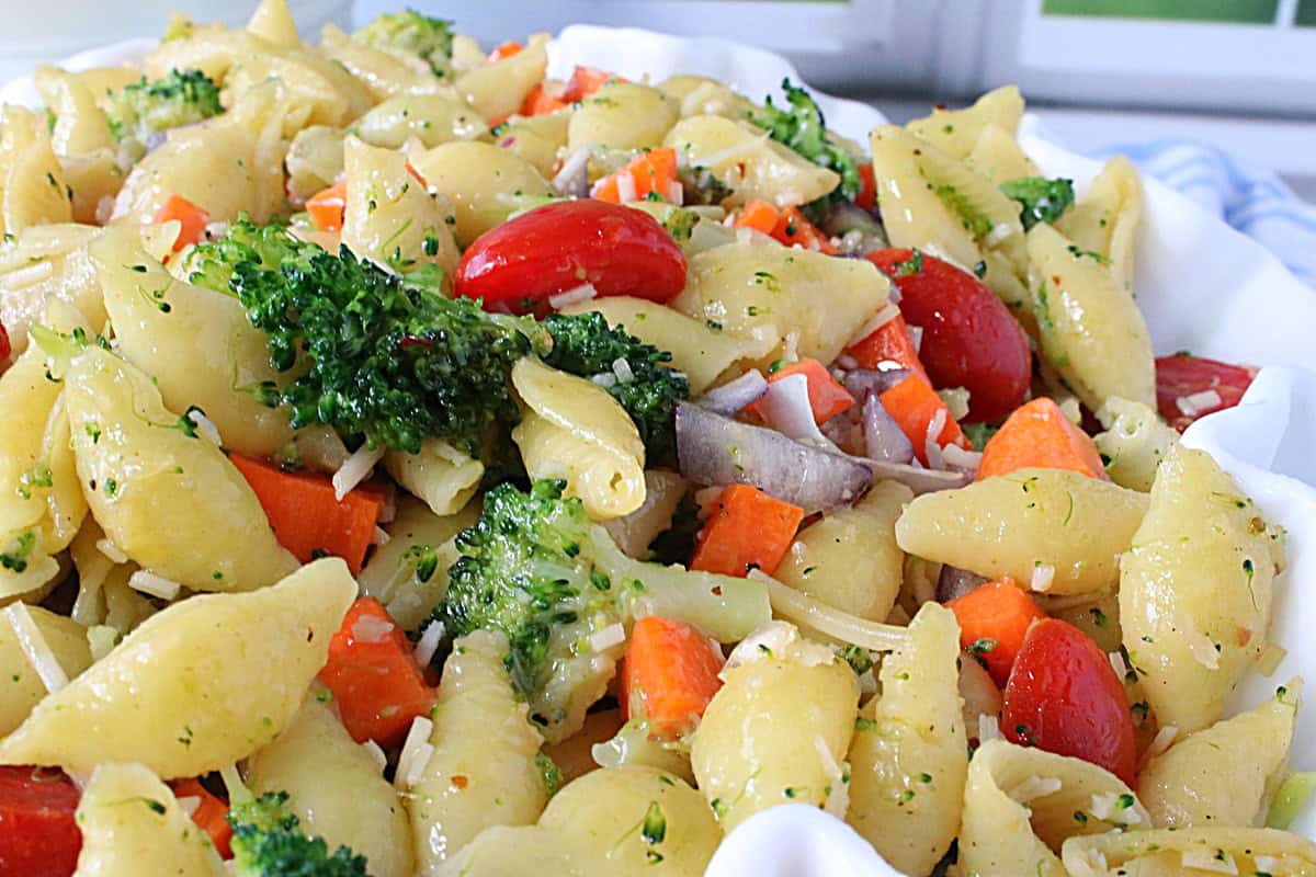 A closeup of cooked shell pasta salad with broccoli, carrots, and tomatoes.