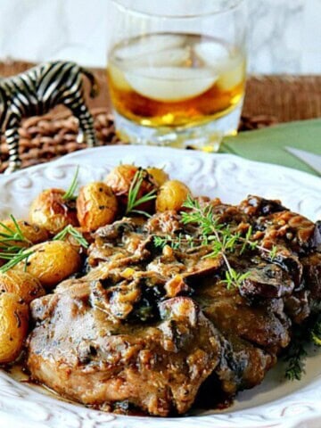 A white plate filled with steak with mushroom bourbon gravy and topped with fresh herbs.