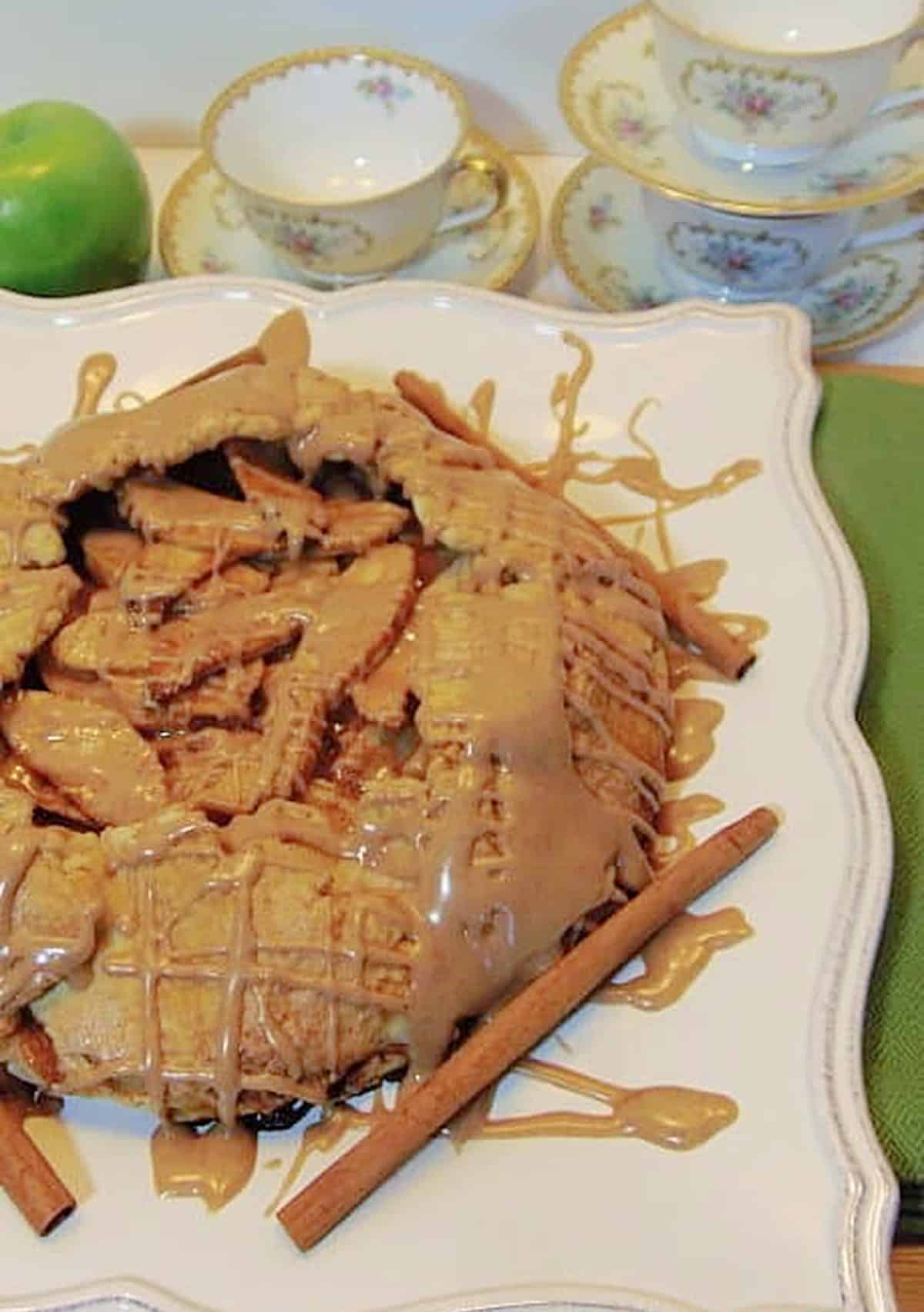 A classic rustic apple crostata on a plate with cinnamon sticks and a cinnamon glaze drizzle.