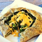 A roasted broccoli crostata topped with cheese sauce on a square plate.