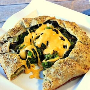 A roasted broccoli crostata topped with cheese sauce on a square plate.