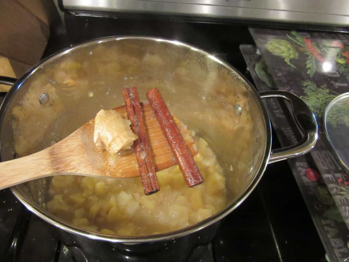 A knob of ginger and two cinnamon sticks being taken from a pot of apple sauce.