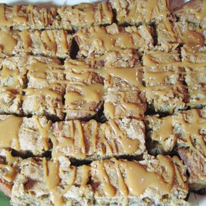 A bunch of Apple Raisin Caramel Cookie Bars on a platter drizzled with caramel and sprinkled with salt.