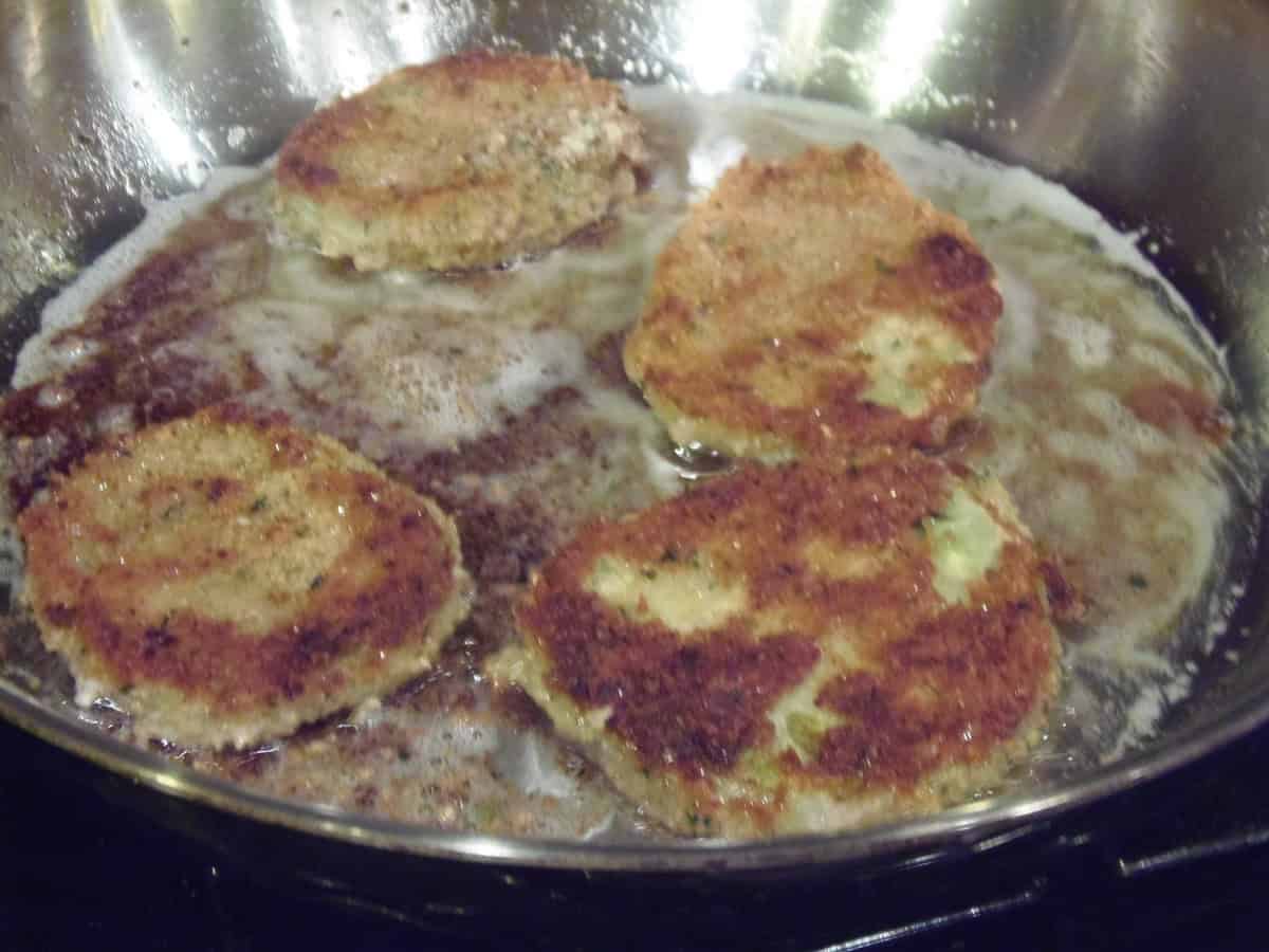 Coated and breaded fried green tomatoes in a skillet with oil.