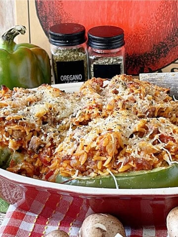 Four Italian Stuffed Bell Peppers in a red casserole dish topped with cheese.