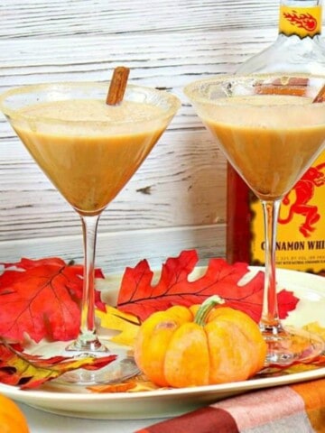 Two martini glasses filled with pumpkin spice martinis along with cinnamon sticks.