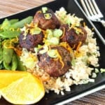 A square black plate with a serving of Asian-Inspired Pork Meatballs over rice on it.