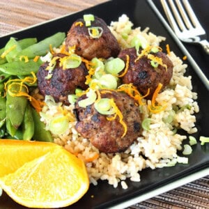 A square black plate with a serving of Asian-Inspired Pork Meatballs over rice on it.