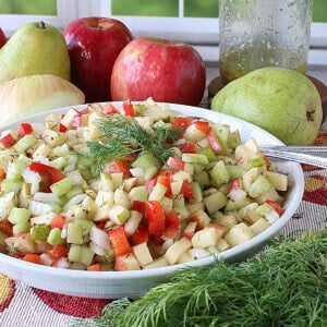 Fresh apples and pears behind a bowl of cucumber and fruit salad.