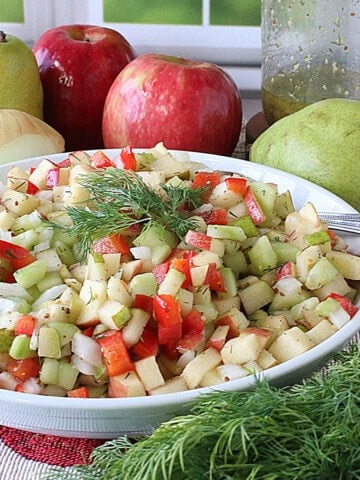 Fresh apples and pears behind a bowl of cucumber and fruit salad.