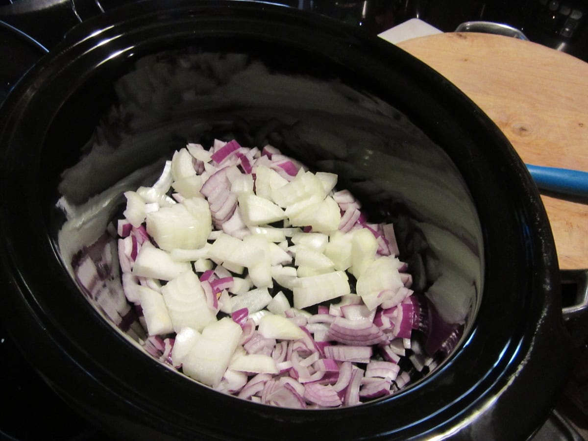 Chopped onions inside a large slow cooker.