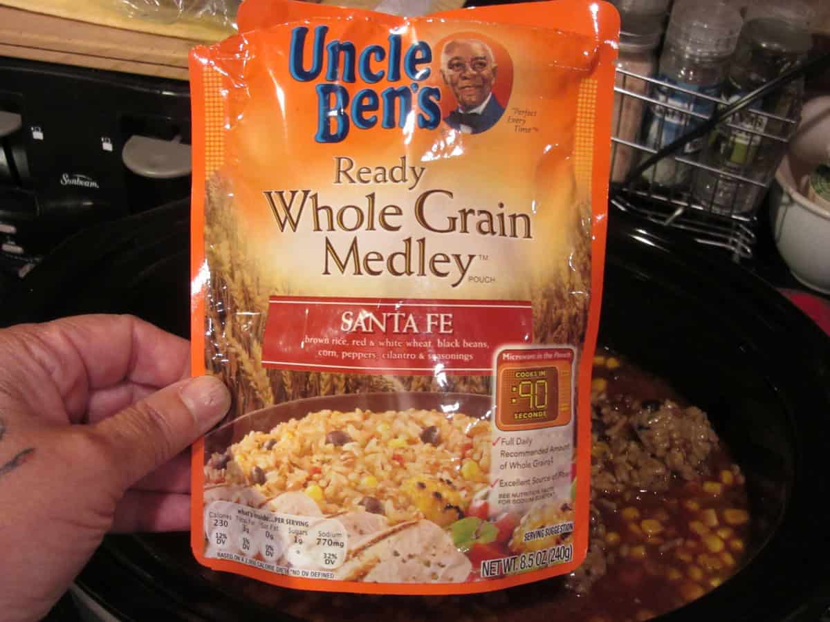 A packet of Uncle Ben's rice being held over a crock pot.