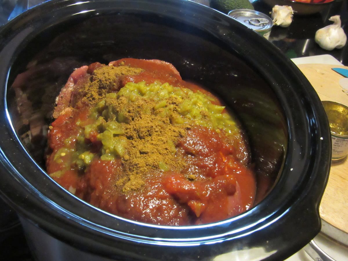 Spices and seasonings in a slow cooker with salsa and pork tenderloin.
