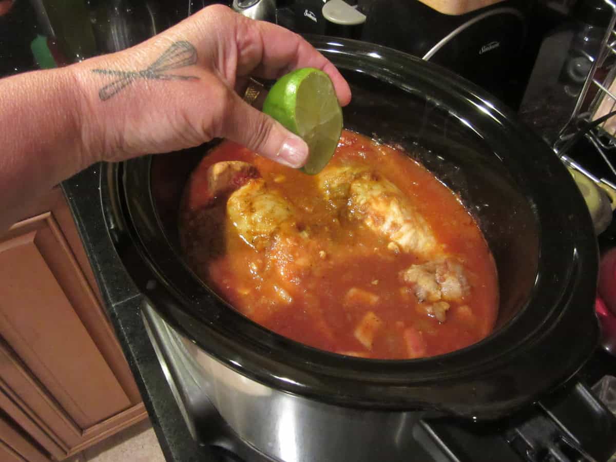 A hand squeezing a lime into a slow cooker.