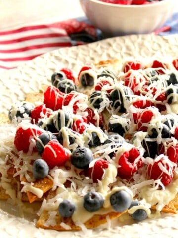 A white platter filled with cinnamon sugar dessert nachos topped with berries.