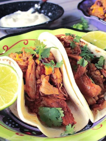 Two slow cooker pulled pork tacos on plate with cilantro and fresh lime.