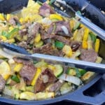A pair of cooking tongs in a skillet with cooked flank steak and squash.