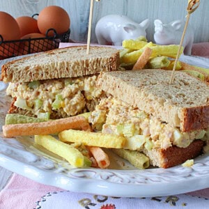 A ham and egg salad sandwich on a pretty white plate.