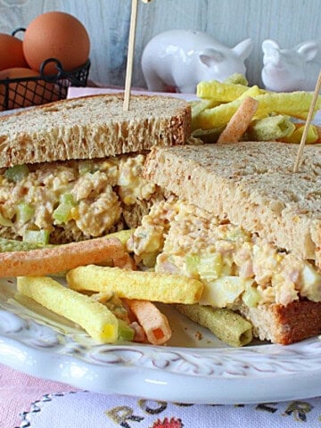 A ham and egg salad sandwich on a pretty white plate.
