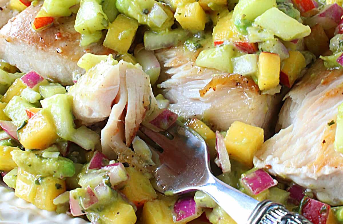 A fork with a bite of seared mahi mahi on the end along with some fruit and vegetable salsa.