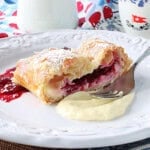 A dollop of cheesecake and cherry filling on a plate with a slice of cherry strudel.