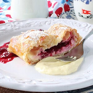 A dollop of cheesecake and cherry filling on a plate with a slice of cherry strudel.