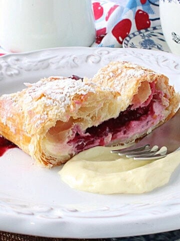 A dollop of cheesecake and cherry filling on a plate with a slice of cherry strudel.