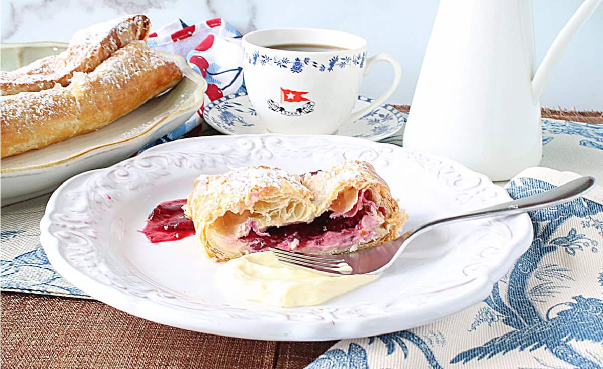 A white plate with a serving of cherry strudel, a fork, and cherry filling.