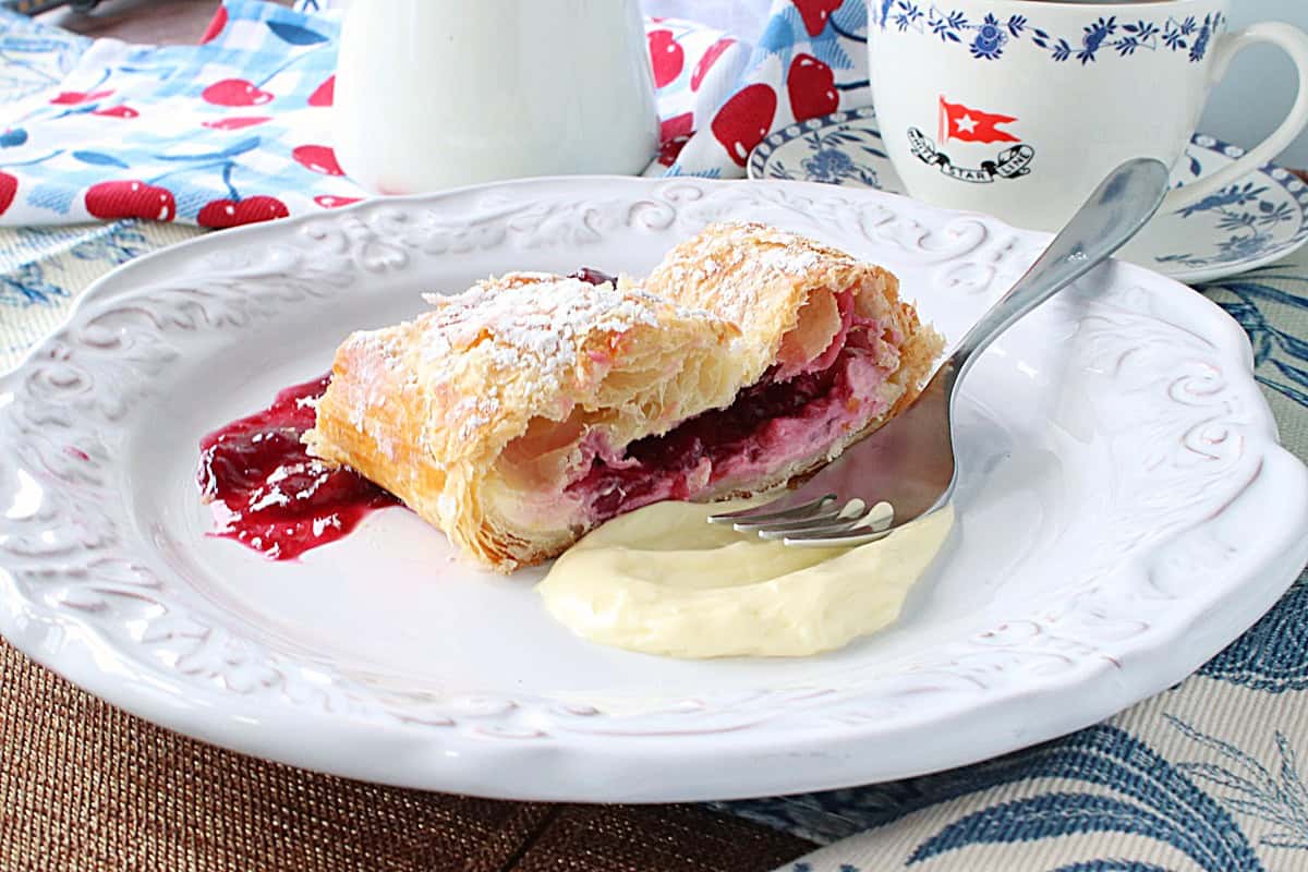 A red, white, and blue table setting for a cherry cheesecake strudel on a plate with a fork.