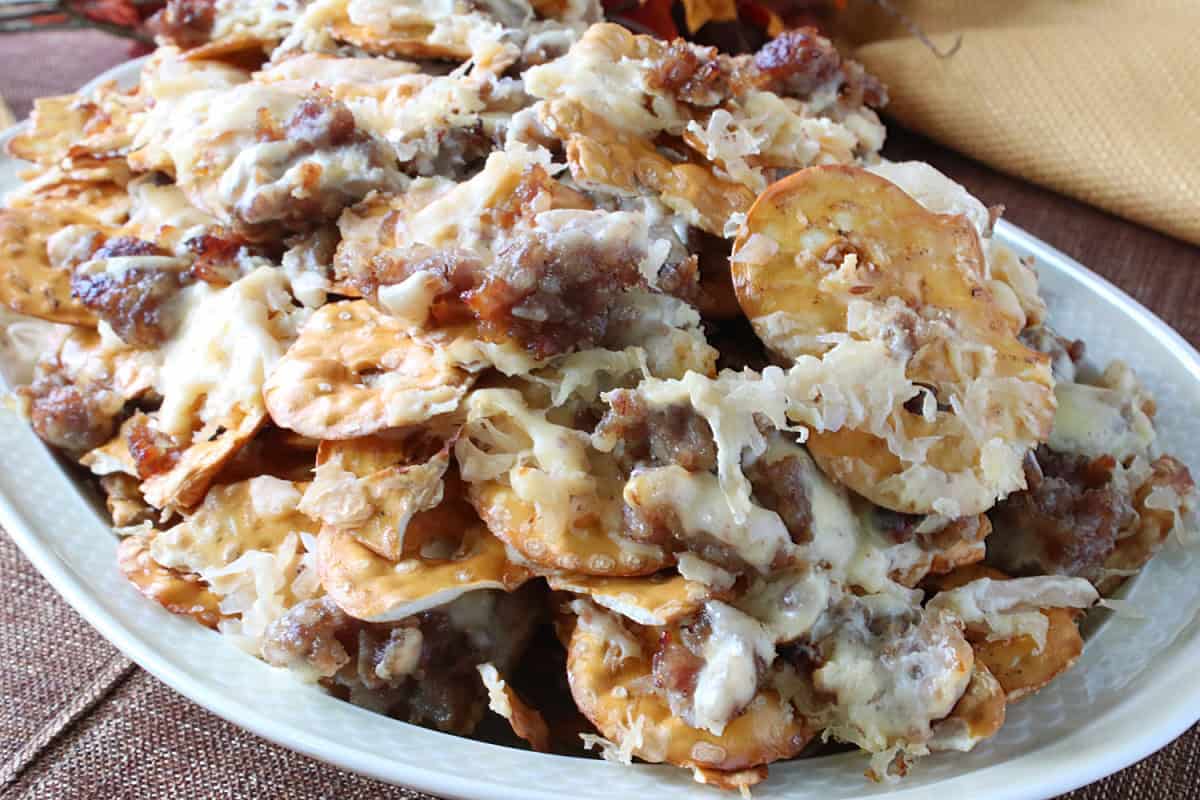 A platter of pretzel chip nachos covered with cooked and crumbled bratwurst, sauerkraut and melted cheese.