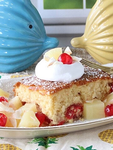 A dollop of whipped cream and a cherry on top of a slice of Piña Colada Dump Cake.
