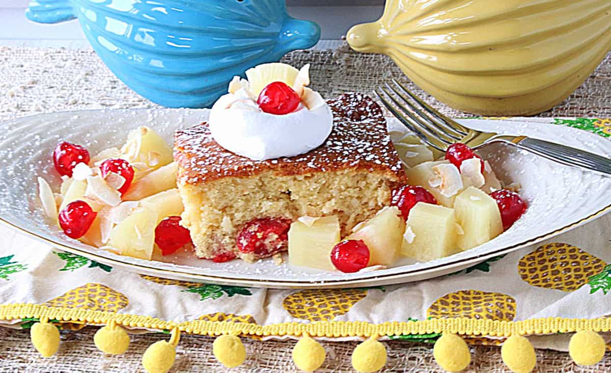 Pineapple chunks and cherries surrounding a slice of Piña Colada Dump Cake on a plate.