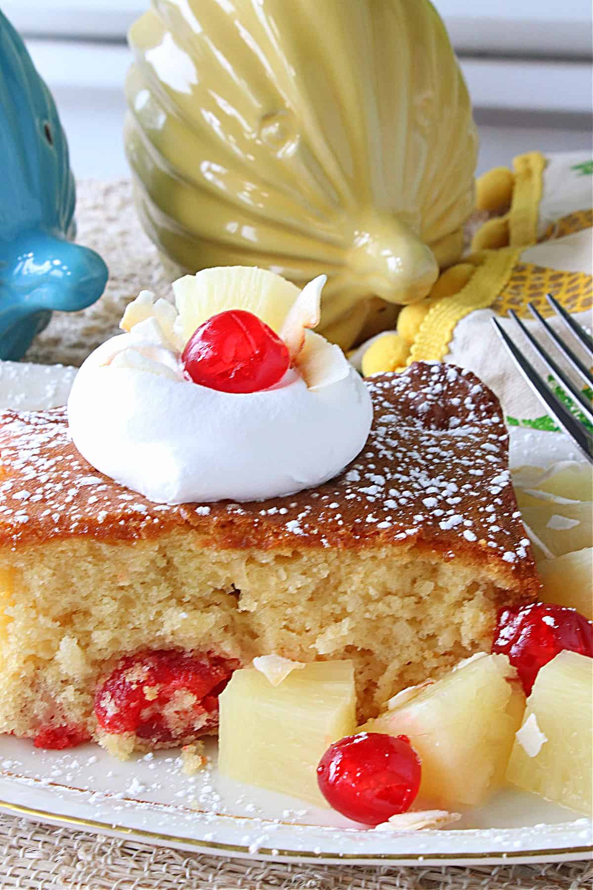 A square of Piña Colada Dump Cake on a platter with pineapple chunks and cherries.