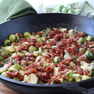 A cast iron skillet filled with sauteed Brussels sprouts with crispy prosciutto.