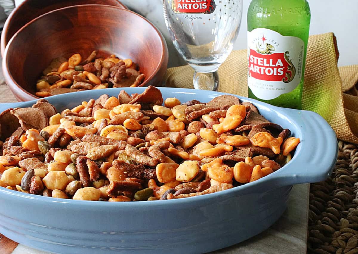 An empty bottle of beer in the background and a blue bowl filled with homemade sesame seed stick snack mix in the foreground.