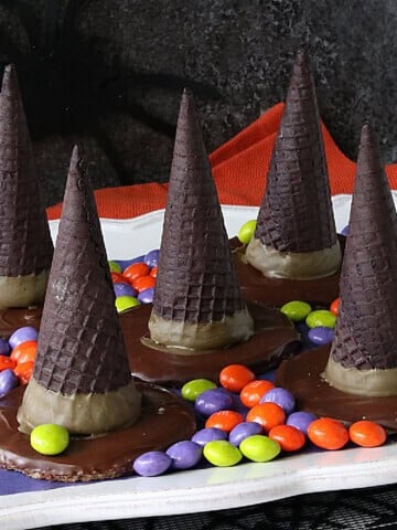 Five candy filled with hat Halloween treats on a platter surrounded by skittles.